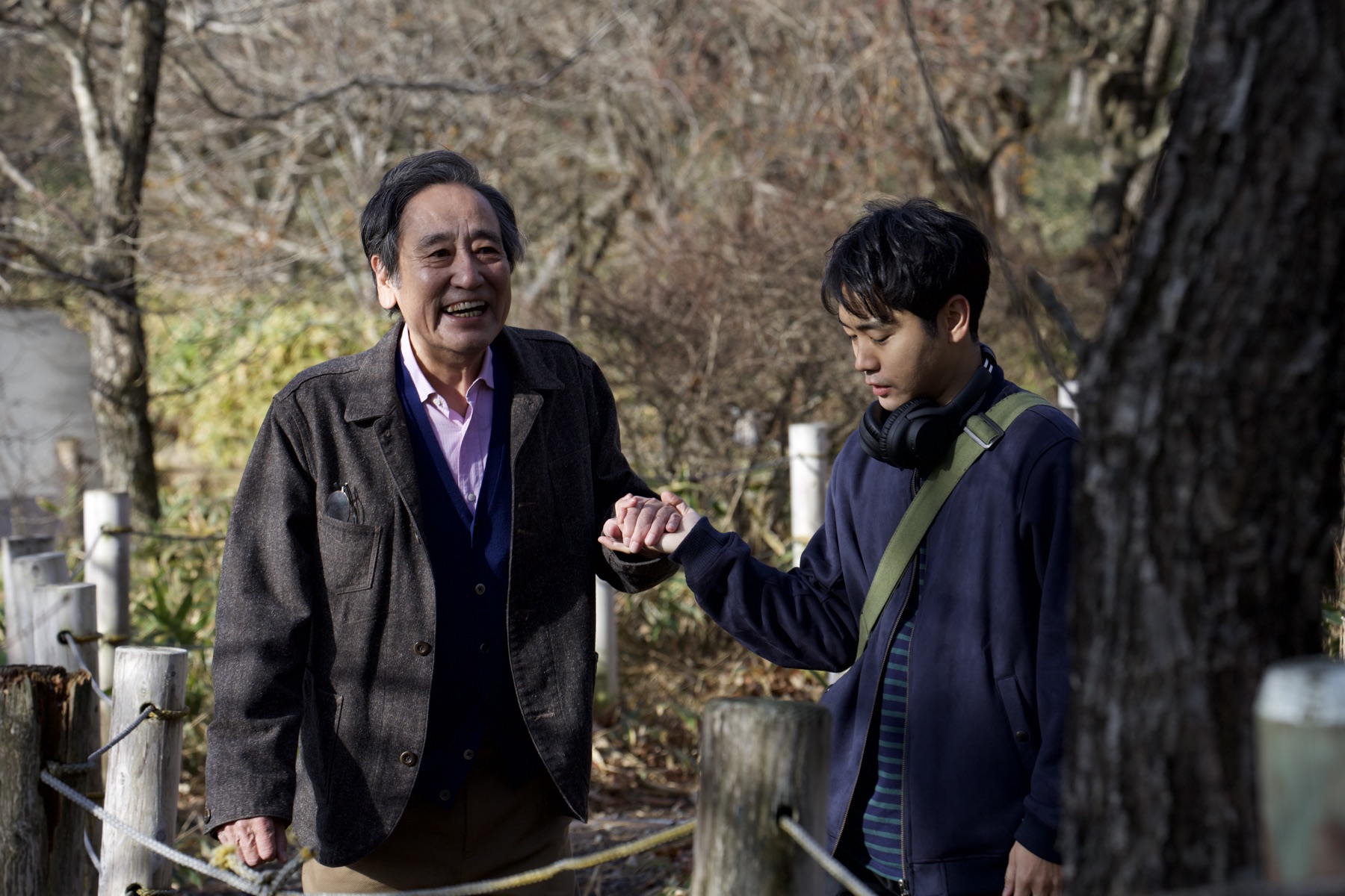 場面写真：木立の小道を並んで歩く豊と優輝。豊が笑い、優輝がその手を取っている。