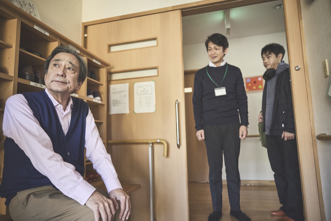 場面写真：施設の居室に座る豊と、戸口に立つ優輝たち。