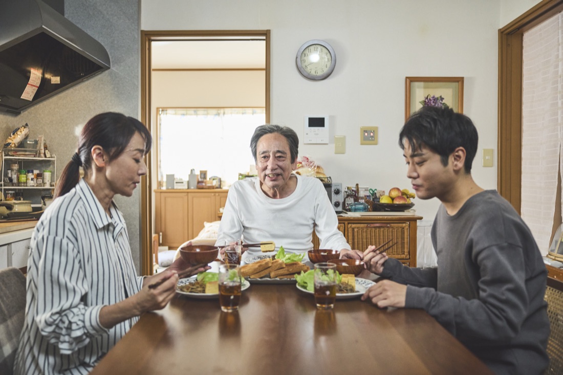 場面写真：食卓を囲む三人。豊と優輝が向かい合って座る。
